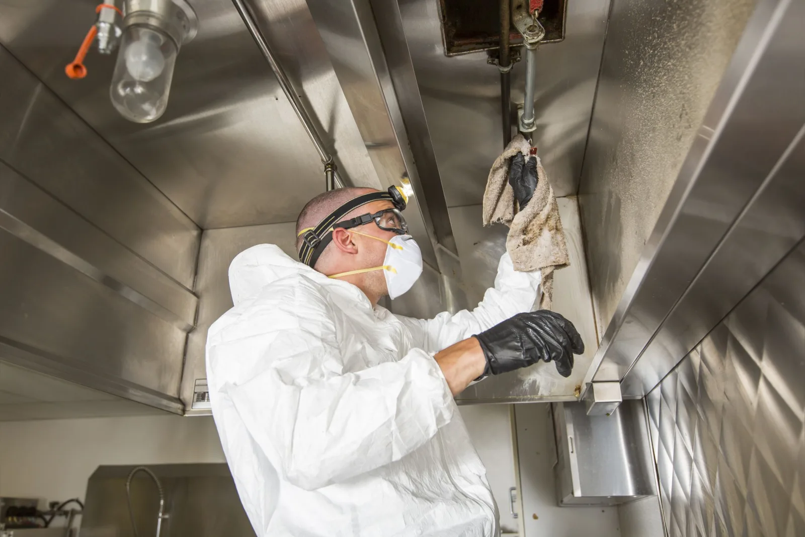 Technician wiping the stainless steel interior of a commercial cooking hood